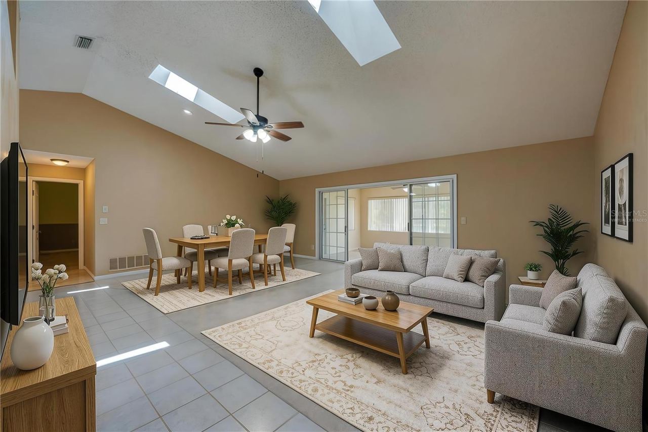 Photo 13 of 20: Virtually Staged - Expansive living room area featuring vaulted ceilings with skylights, carpeted flooring, and sliding glass doors that open to a sun room.