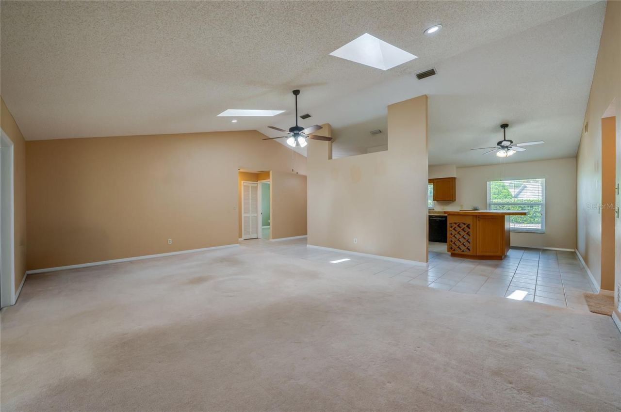 Photo 11 of 20: Open-concept living space highlighting high vaulted ceilings, skylights, plush carpeting, and seamless flow into the adjacent tiled kitchen area.