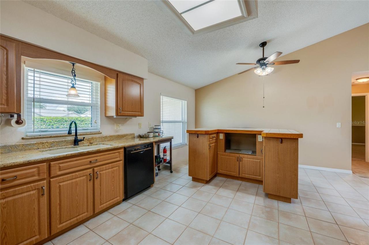 Photo 10 of 20: Bright kitchen featuring warm wood cabinetry, neutral countertops, a ceiling fan, and durable tile flooring throughout.