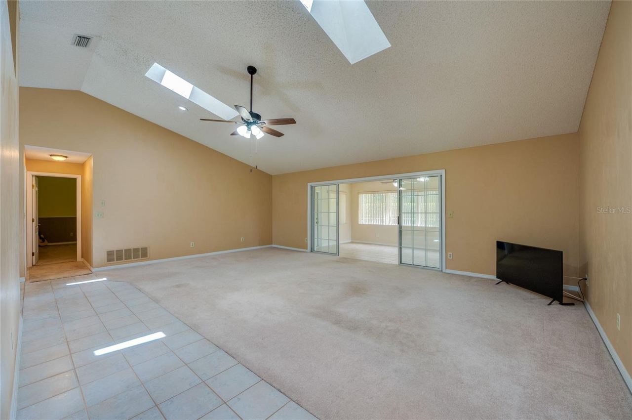 Photo 12 of 20: Expansive living room area featuring vaulted ceilings with skylights, carpeted flooring, and sliding glass doors that open to a sun room.