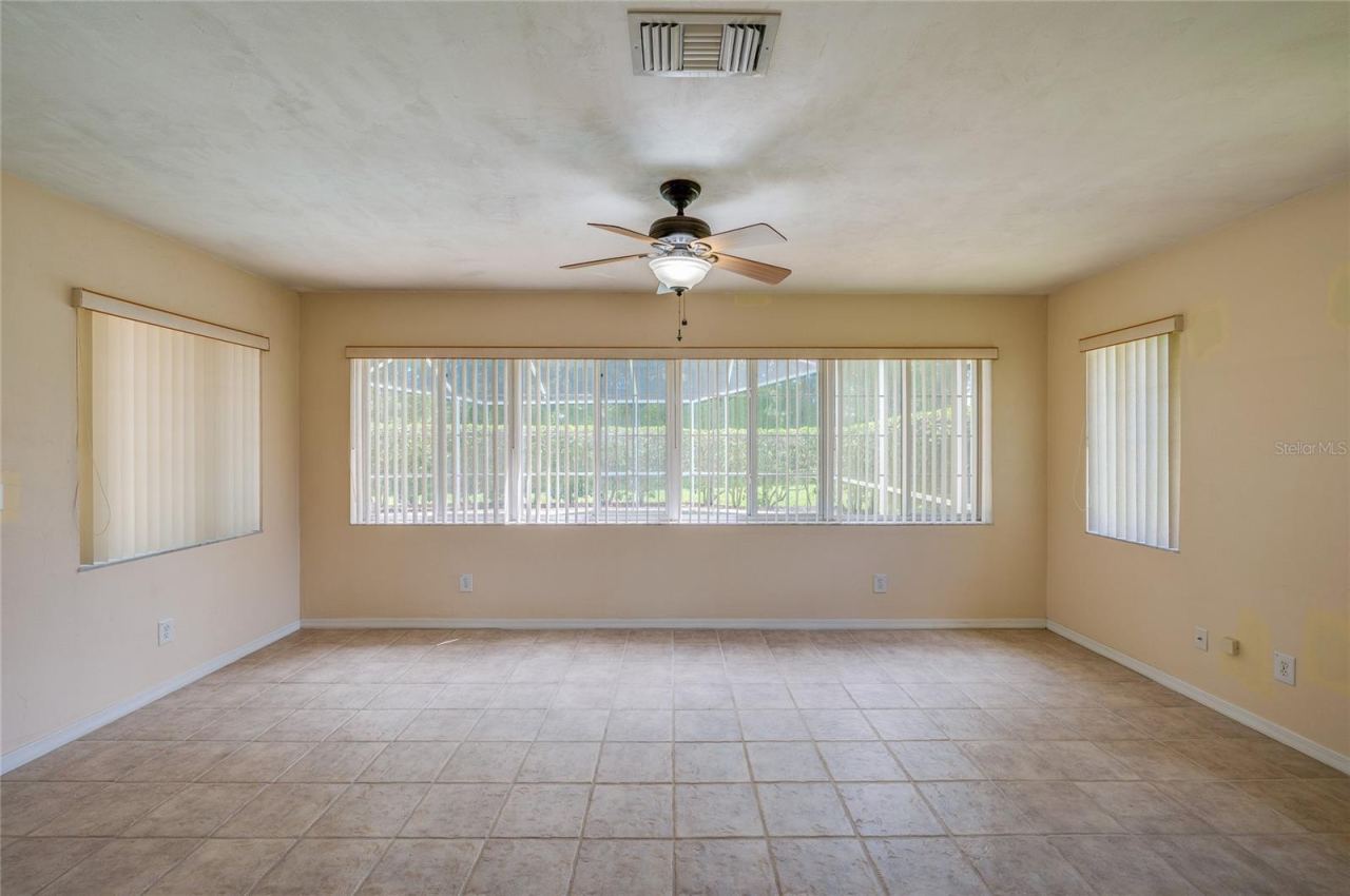 Photo 14 of 20: Bright enclosed sunroom equipped with light beige tile flooring, a ceiling fan, and wide windows fitted with vertical blinds for controlled light.