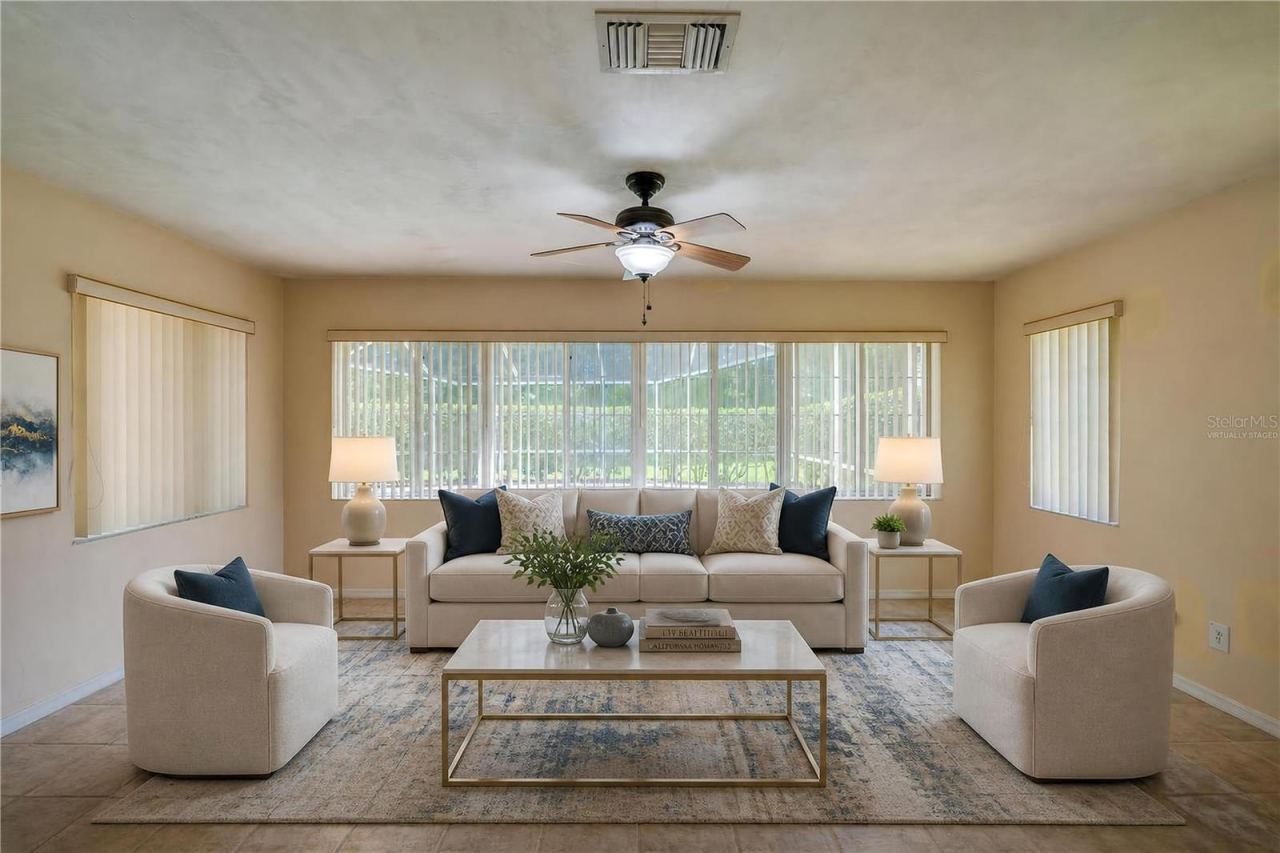 Photo 15 of 20: Virtually Staged - Bright enclosed sunroom equipped with light beige tile flooring, a ceiling fan, and wide windows fitted with vertical blinds for controlled light.