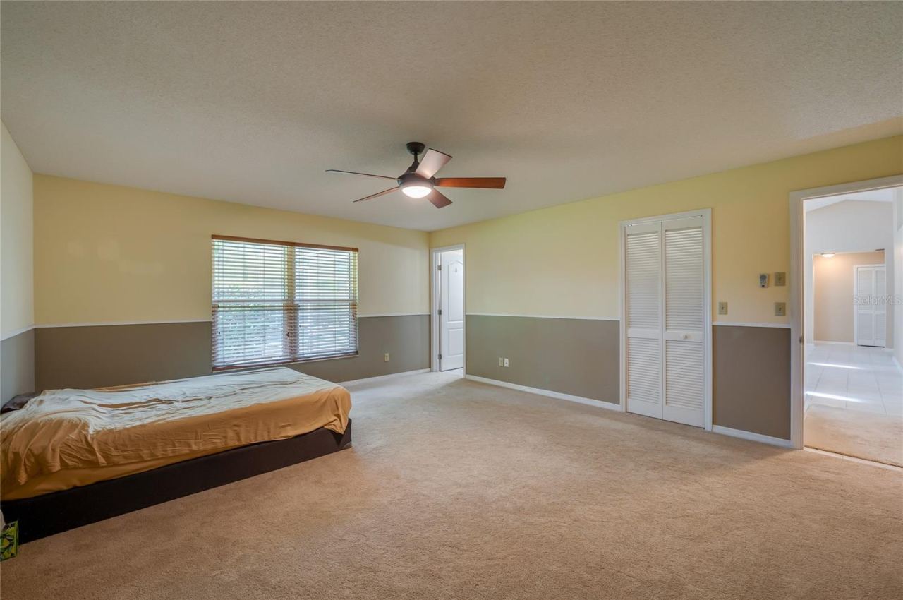 Photo 19 of 20: Generously sized bedroom offering wall-to-wall carpeting, two-tone neutral walls, a ceiling fan light fixture, and louvered closet doors.